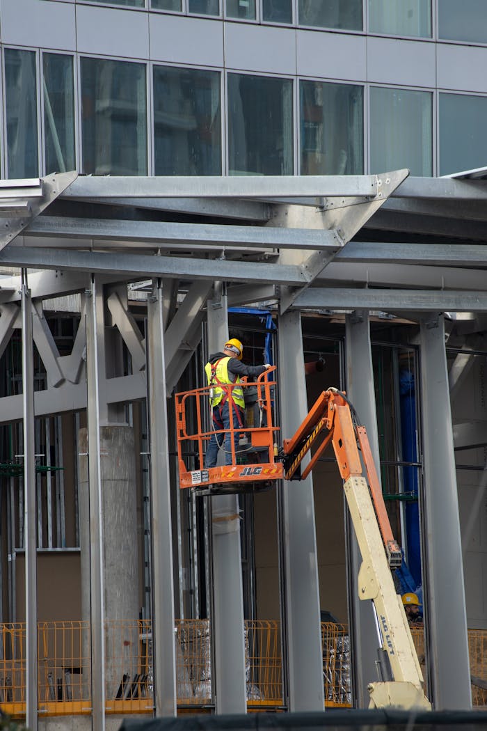 Anasayfa Construction worker operating aerial lift during urban building project with steel structures.