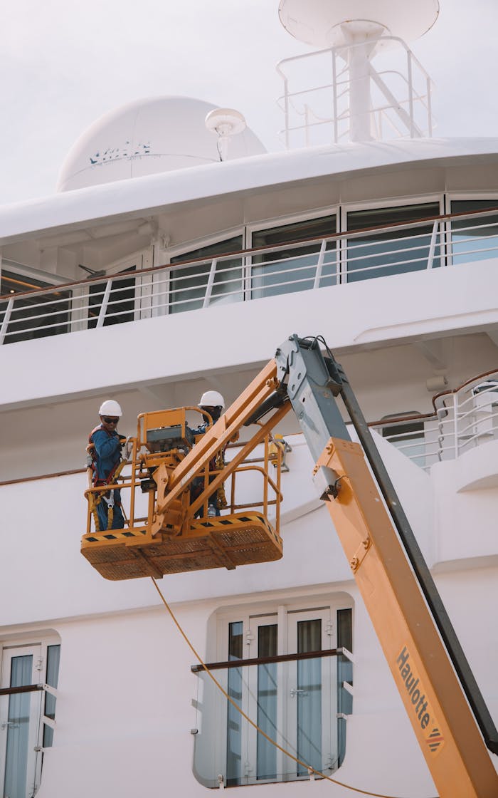 Anasayfa Two workers on a scissor lift performing maintenance on a cruise ship in Málaga, Spain.