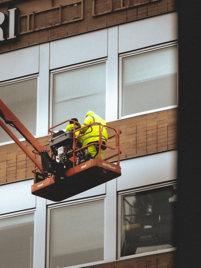 Anasayfa Two workers on a cherry picker doing maintenance on a building façade.