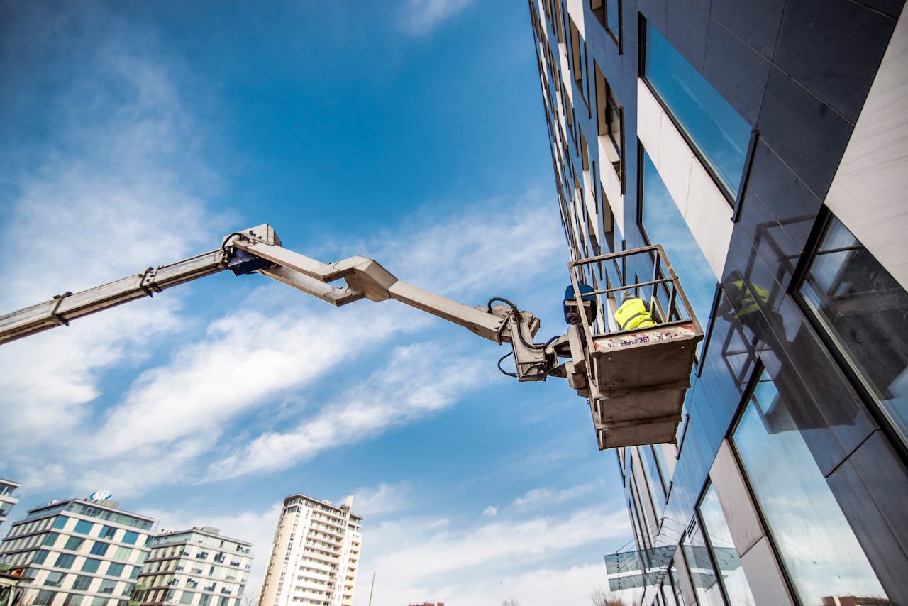 Anasayfa Construction worker on a lift near high-rise building against blue sky.